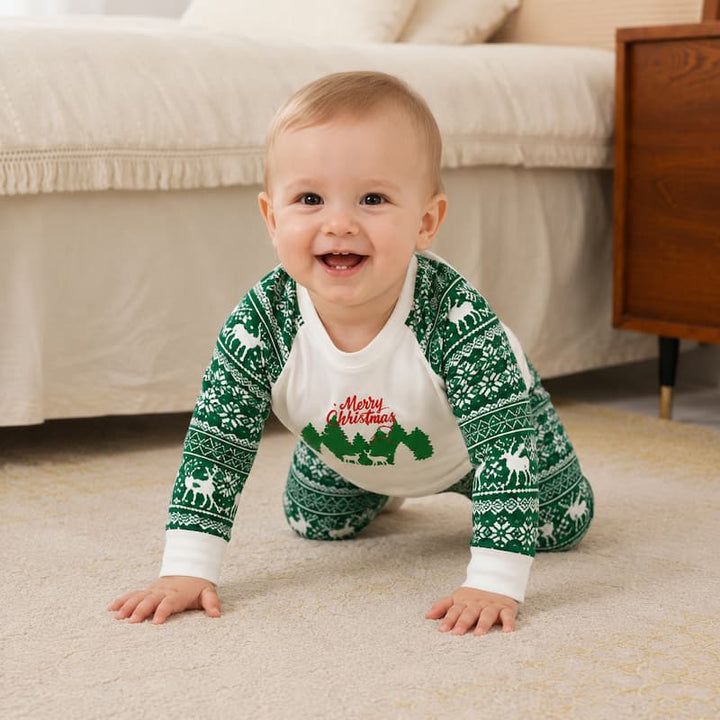 A baby crawling on a beige carpet in a bedroom, wearing a green and white Christmas-themed long-sleeve pajama top with a white belly panel that says 'Merry Christmas' in red script.