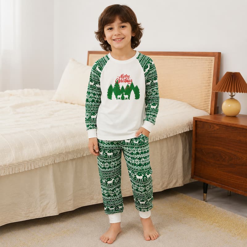 A child wearing a long-sleeve Christmas pajama set with a white crewneck top and green patterned pants, standing in a bedroom setting.